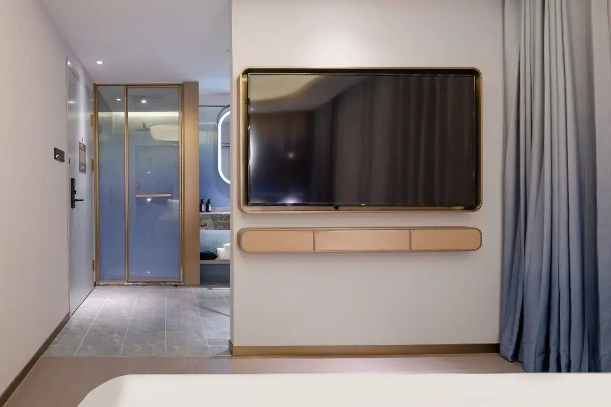 A modern hotel room with a large window, a built-in desk, and a sliding glass door leading to a bathroom.