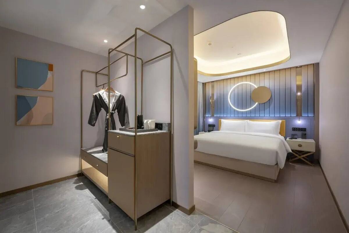 Una habitación de hotel moderna con cama, mesita de noche y armario con espejo.