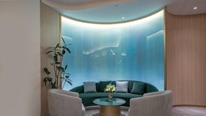 En moderne lobby med et buet siddeområde, et glasbord og en stor plante.