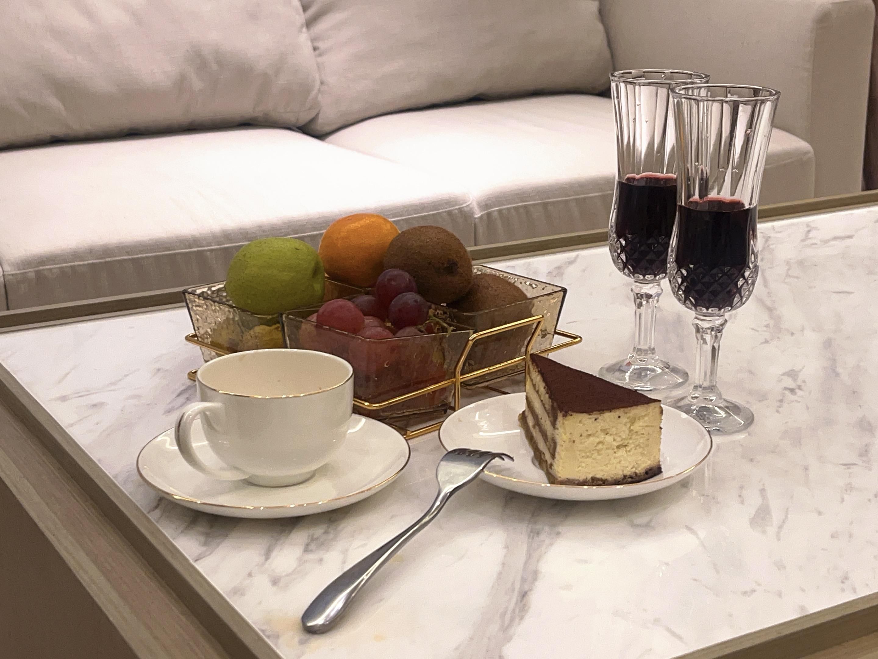 Una mesa de mármol con un postre, un frutero y copas de vino tinto.