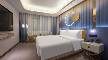 A modern hotel room with a large bed, bedside table, and a wall-mounted TV.