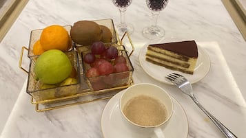 A marble table with a fruit basket, a slice of cake, two glasses of red wine, a cup of coffee, and a fork.