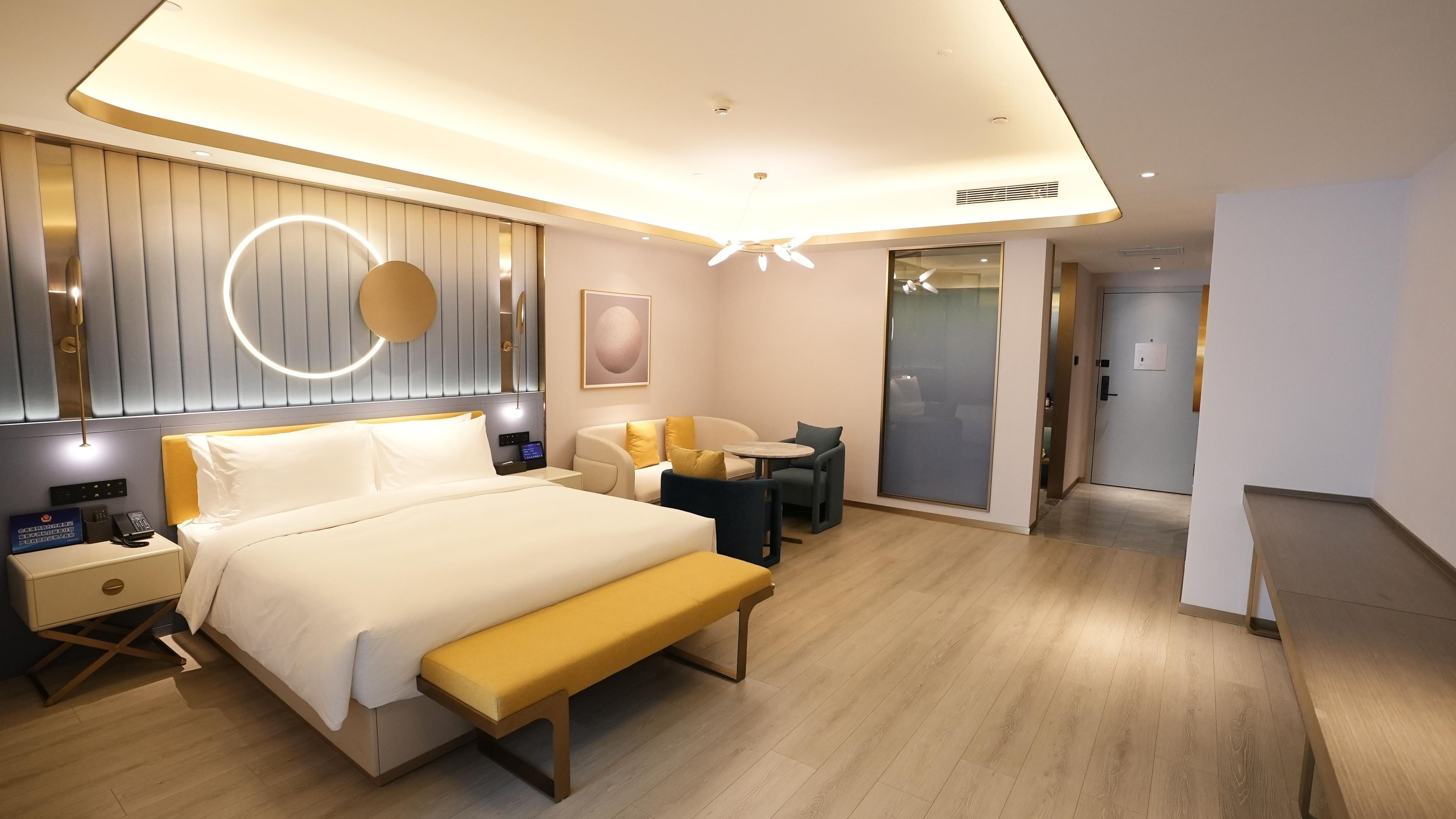 A modern hotel room with a bed, bedside table, lamp, and a bench.