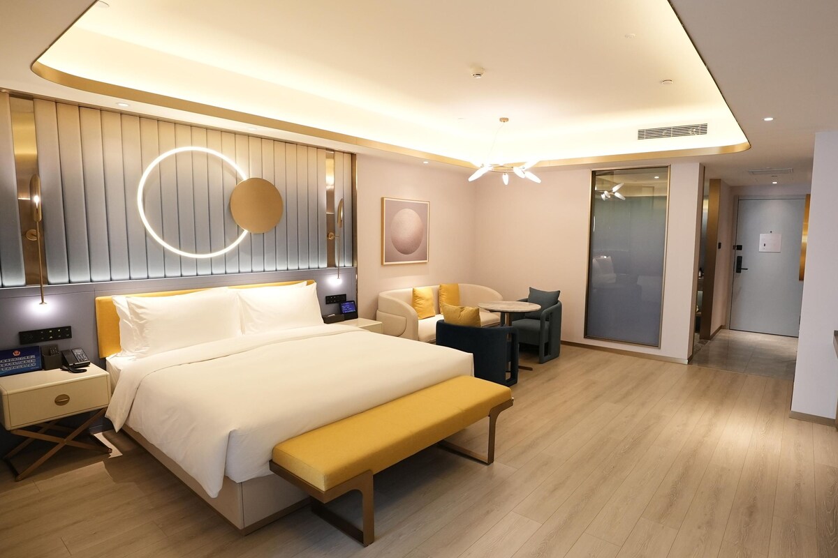 A modern hotel room with a bed, bedside table, lamp, and a bench.