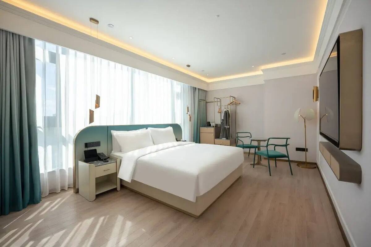 Una habitación de hotel moderna con una cama grande, una mesita de noche con teléfono, un escritorio con silla y un televisor en la pared.