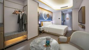 Ein modernes Hotelzimmer mit Bett, Nachttisch, rundem Couchtisch, einer Sitzecke, einem Kleiderschrank mit Kleidung und einer runden Wandleuchte.