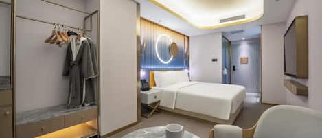 A modern hotel room with a bed, bedside table, a round coffee table, a seating area, a wardrobe with hanging clothes, and a circular light fixture on the wall.