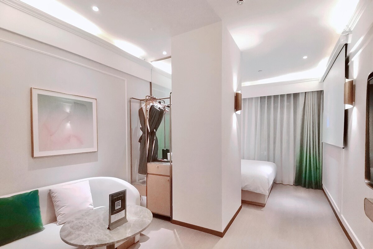 Una habitación de hotel moderna con una cama, un área de descanso con una mesita, un espejo y un armario.