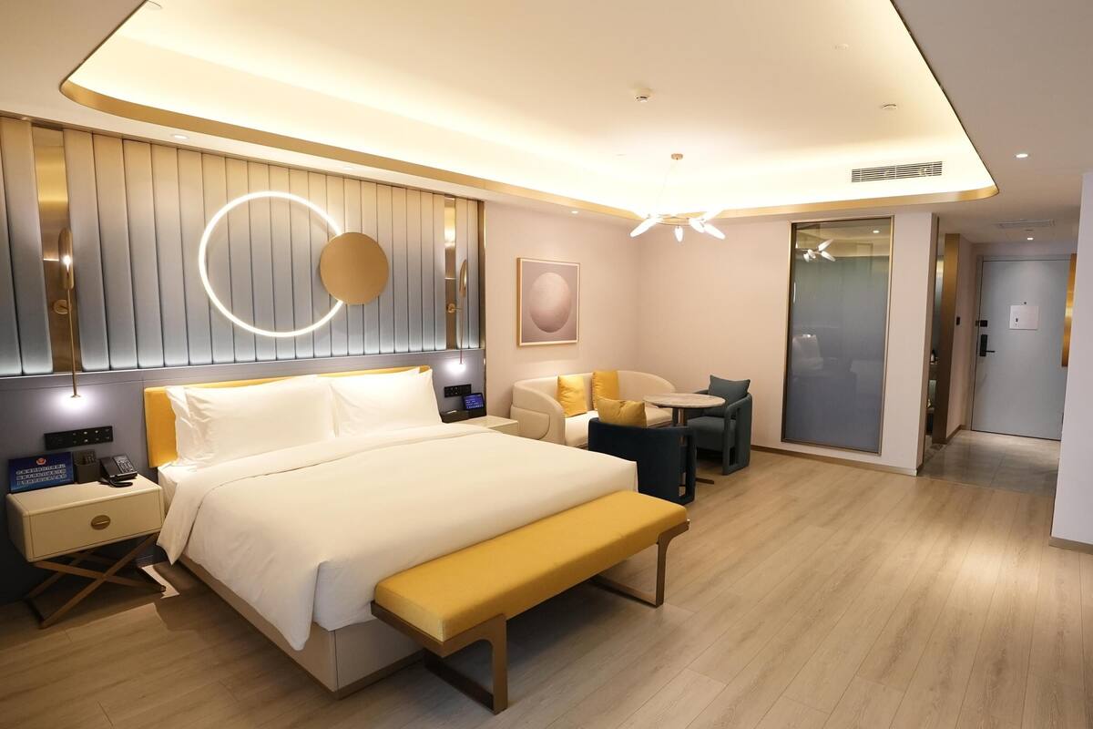 Una habitación de hotel moderna con cama, mesita de noche, lámpara y un banco.