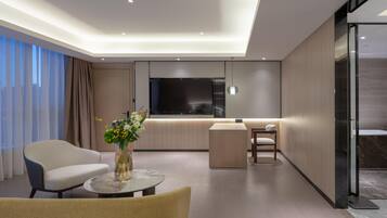 A modern hotel room with a sofa, a round coffee table, a TV, and a glass partition.