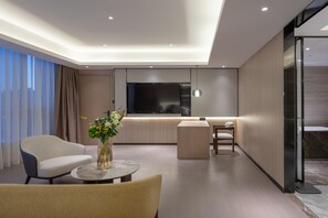 Una habitación de hotel moderna con un sofá, una mesa redonda de centro, un televisor y un separador de vidrio.