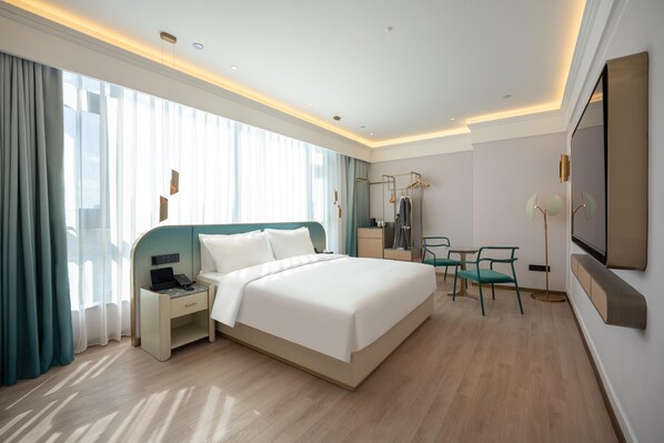 A modern hotel room with a large bed, bedside table, desk, chairs, and a TV. - Madison Hotel Beijing Olympic Center Bird's Nest (Beijing)