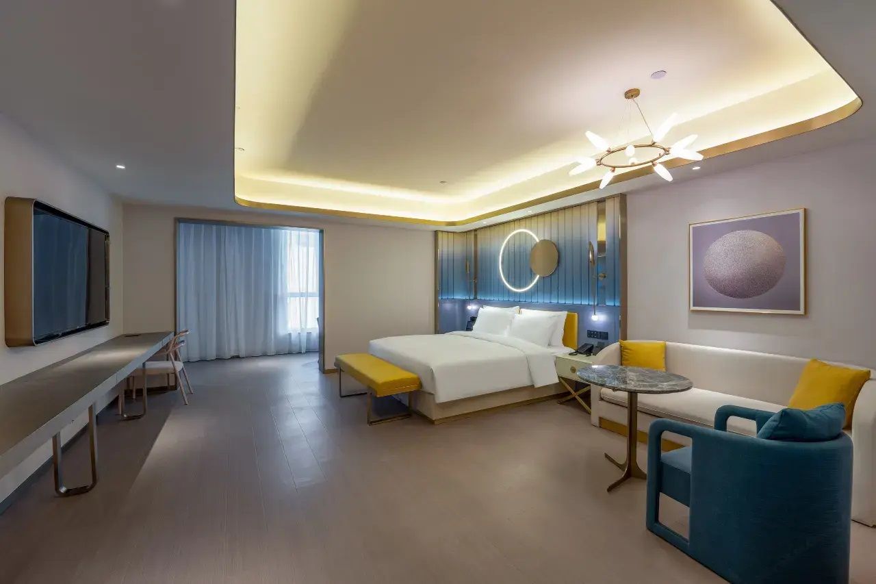 A modern hotel room with a bed, a sofa, a small table, a bench, and a TV.