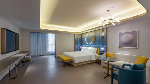 Ein modernes Hotelzimmer mit Bett, einer Couch, einem kleinen Tisch, einer Bank und einem Fernseher.