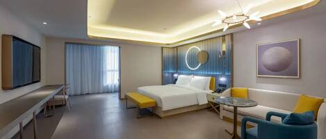 A modern hotel room with a bed, a sofa, a small table, a bench, and a TV.