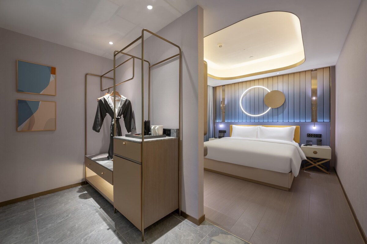 Una habitación de hotel moderna con una cama, un armario, un espejo y una lámpara circular fijada en la pared.