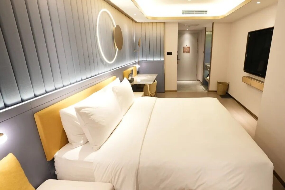 Ein modernes Hotelzimmer mit einem großen Bett, Nachttischen, einem Fernseher und einem durch eine geöffnete Tür einsehbaren Badezimmer.