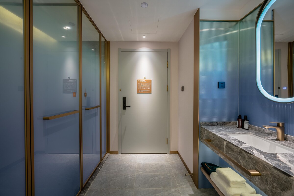 Un baño moderno con puerta de vidrio, lavamanos de mármol y un perchero para toallas.