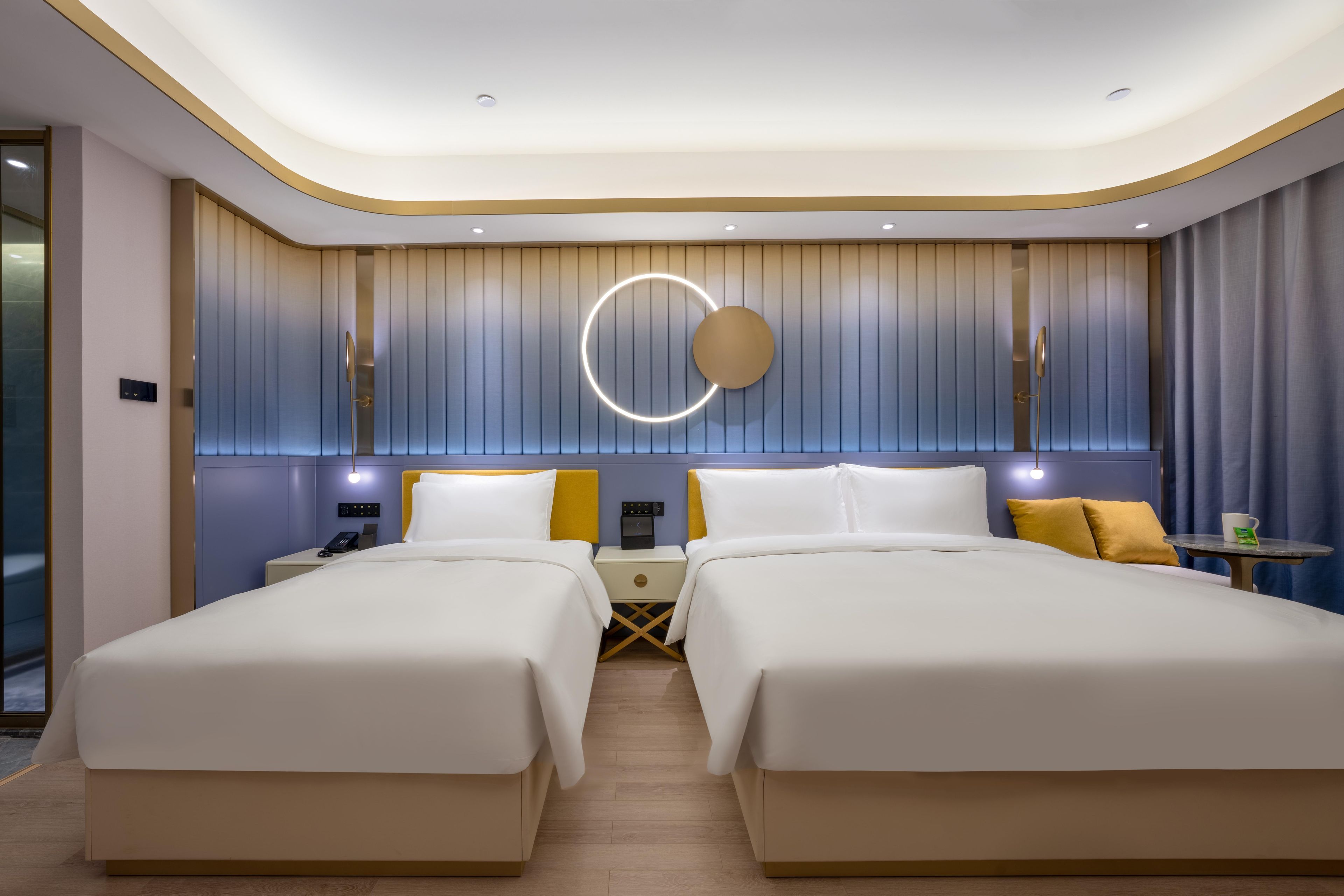 Ein modernes Hotelzimmer mit zwei Betten, einer runden Leuchte, einem kleinen Tisch und einem Nachttisch.