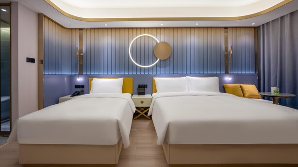 Una habitación de hotel moderna con dos camas, una lámpara redonda, una mesita pequeña y una mesita de noche.