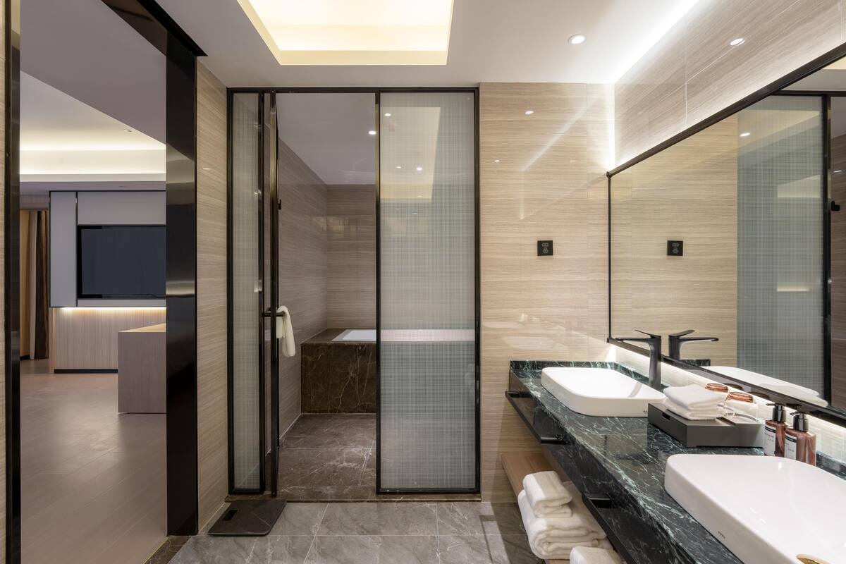 Un baño moderno con cabina de ducha de vidrio, lavamanos dobles y un espejo grande.