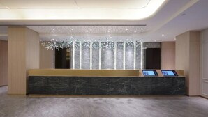 Un mostrador de recepción con encimera de mármol, dos quioscos digitales y un elegante candelabro.