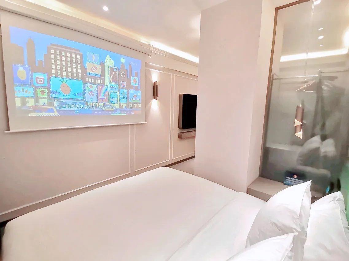 Ett hotellrum med en säng, en TV som är monterad på väggen och en duschkabin med glasväggar.