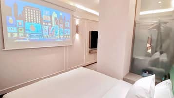 Ett hotellrum med en säng, en TV som är monterad på väggen och en duschkabin med glasväggar.