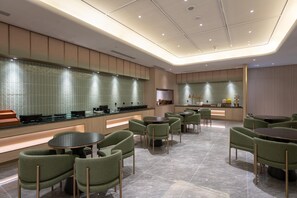 Un restaurante moderno con una barra larga, sillas tapizadas en verde y un revoque de azulejos.