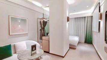 Moderni hotellihuone, jossa on sohva, pieni pyöreä pöytä, sänky, vaatekaappi ja peili.