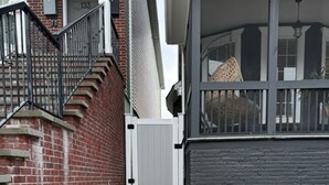 A narrow stairway leading to a porch with a white gate, a brick wall, and a stone pathway.