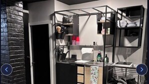 A compact kitchen with a black countertop, wooden cabinets, and a black brick accent wall.