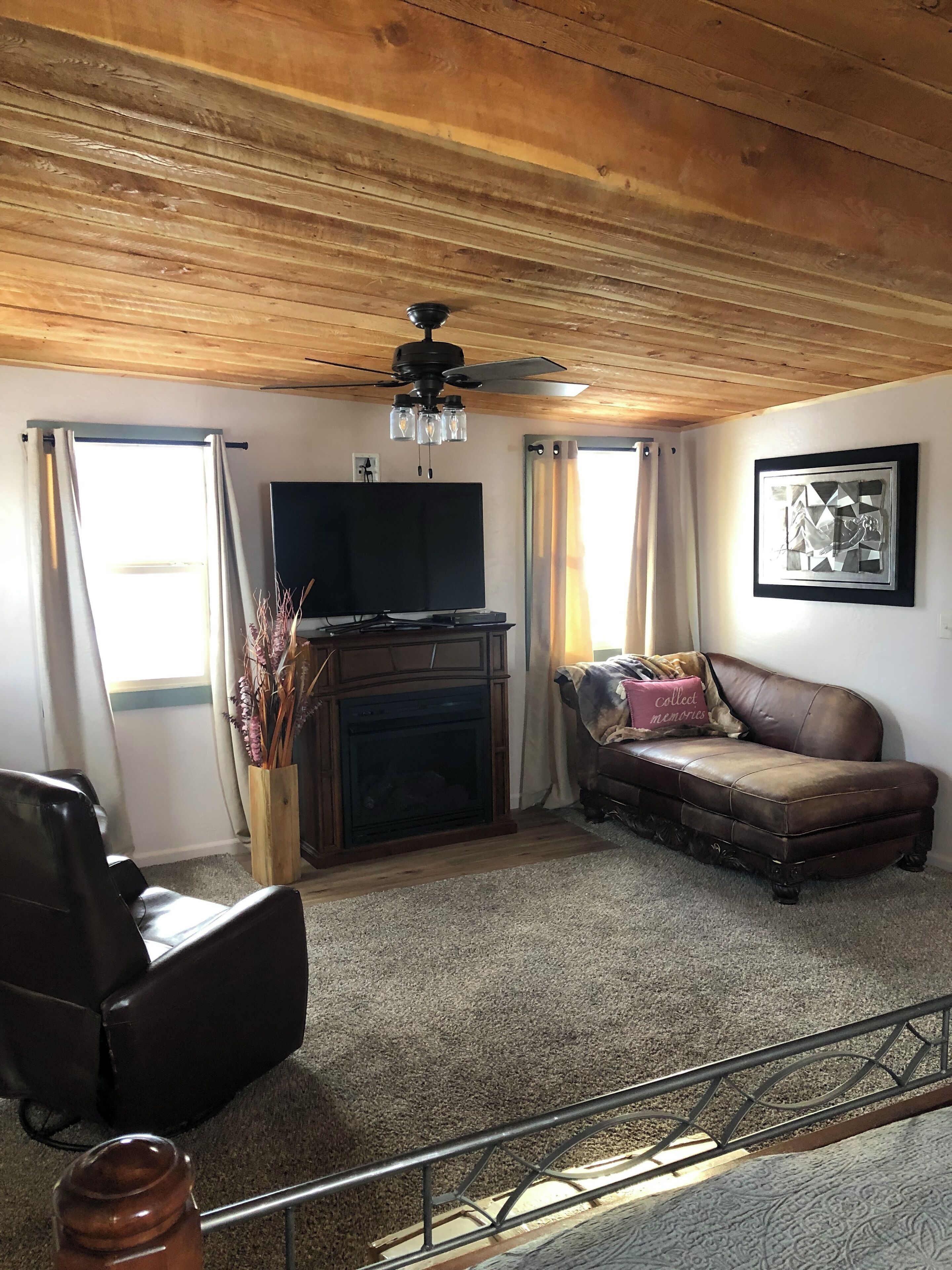 A living room with a fireplace, a television, a brown leather sofa, and a ceiling fan.