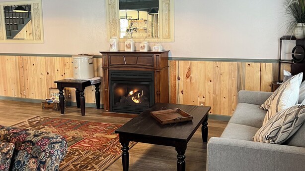 A cozy living room with a fireplace, wooden walls, a sofa, and a patterned rug.