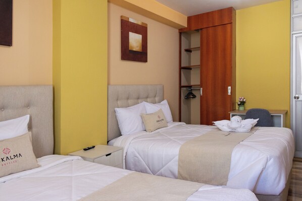 A hotel room with two beds, a wooden wardrobe, a small desk, and a mirror on the wall.