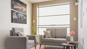 A modern living room with two grey sofas, a small round table with a vase of flowers, and artwork on the wall. - Inkalma sede Don Bosco (Arequipa)