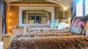 A cozy room with a large mirror, wooden beams, and a bed with a furry blanket.