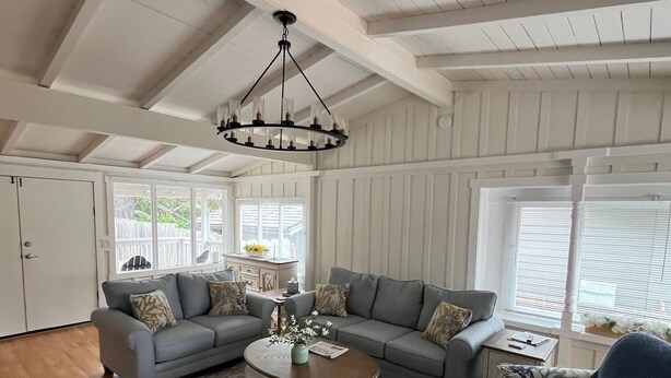 A spacious living room with a high ceiling, a chandelier, a grey sofa set, a round coffee table, and a patterned rug.