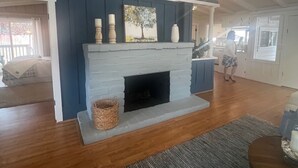 A living room with a fireplace, wooden flooring, and a large window.
