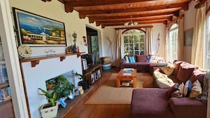 Un salon chaleureux avec un plafond en bois, une cheminée, un ensemble de canapés et une grande fenêtre donnant sur un paysage verdoyant.