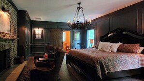 Une chambre à coucher avec un grand lit, une cheminée, un lustre et un coin salon avec des fauteuils.