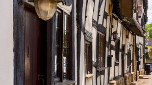 A narrow street lined with traditional half-timbered buildings with exposed wooden beams and white plaster walls. - Pass the Keys | Dara Cottage | 16th Century Thatched Cottage (Mickleton)