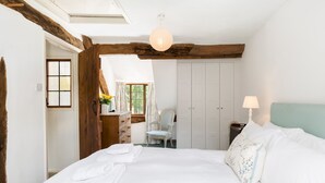 A bedroom with a large bed, a wooden ceiling beam, a skylight, a desk with a chair, and a wardrobe. - Pass the Keys | Dara Cottage | 16th Century Thatched Cottage (Mickleton)