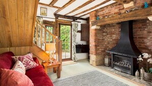 A cozy living room with a fireplace, wooden beams, and a staircase leading to another level. - Pass the Keys | Dara Cottage | 16th Century Thatched Cottage (Mickleton)