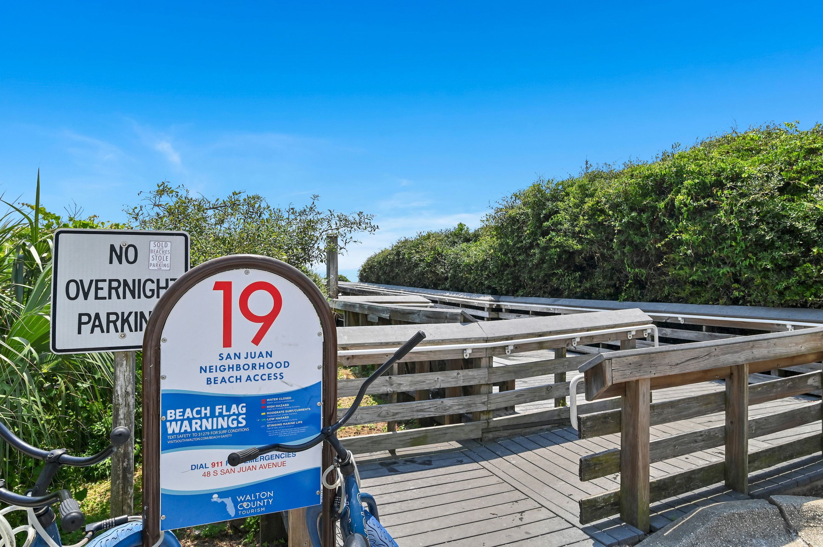 A beach access sign with a number 19, a no overnight parking sign, and a beach flag warning sign.