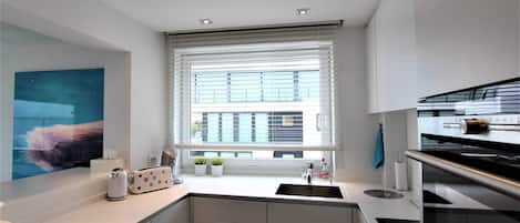 A modern kitchen with a built-in oven, a sink, and a window with blinds.