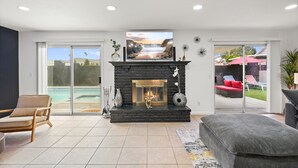 A modern living room with a fireplace, a large window overlooking a pool, and a sliding glass door leading to an outdoor area.