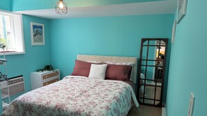 A bedroom with a bed, a nightstand, a dresser, a window, and a hanging light fixture.