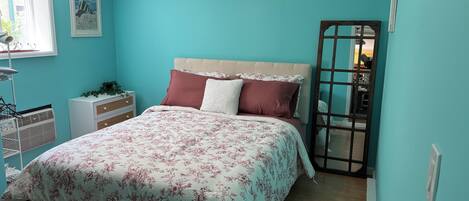 Une chambre à coucher comprenant un lit, une table de chevet, une commode, une fenêtre et un luminaire suspendu.