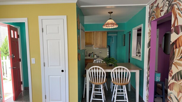 A kitchen with a dining area, wooden cabinets, a hanging light fixture, and a door leading to another room.